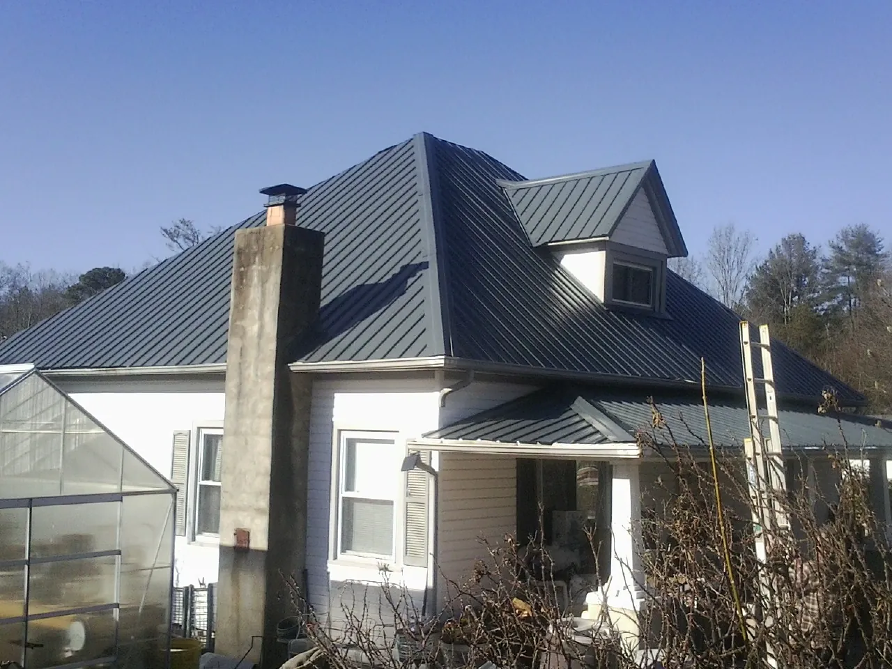 Dark blue standing seam metal roof on a white farmhouse with dormer — Slate & Tile Roof Repair by Roofing Brothers in Holgate
