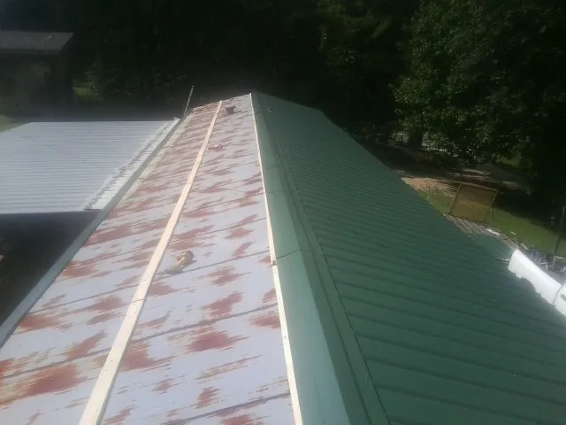 Old rusted panels beside newly installed green metal roofing — Wind Damage Roof Repair by Roofing Brothers in Holgate