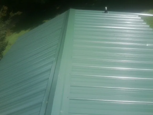 New green metal panels meeting at the ridge of a roof — Flat Roof Repair work by our crew in Holgate