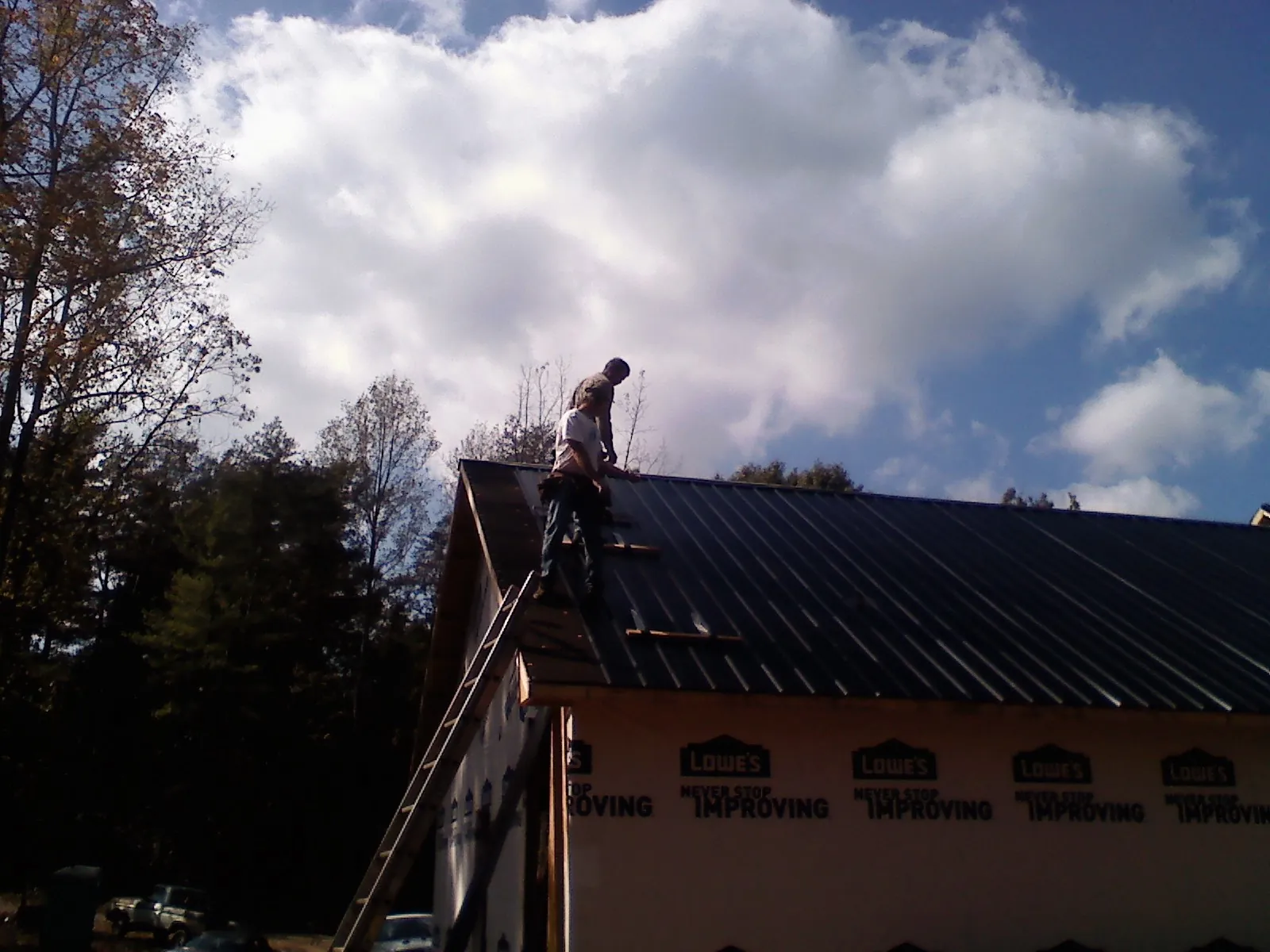 Roofer fastening dark metal panels high against a cloudy sky, from a Roof Inspection job in Holgate